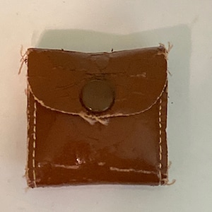 May include: A small brown leather pouch with a single button closure. The pouch is stitched with white thread.
