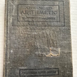 May include: A vintage, gray, cloth-bound book titled "Advanced Arithmetic" with the words "California State Series" printed on the bottom.