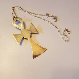 May include: A gold-toned Ankh pendant necklace with a silver chain. The Ankh is a symbol of eternal life in ancient Egyptian mythology.