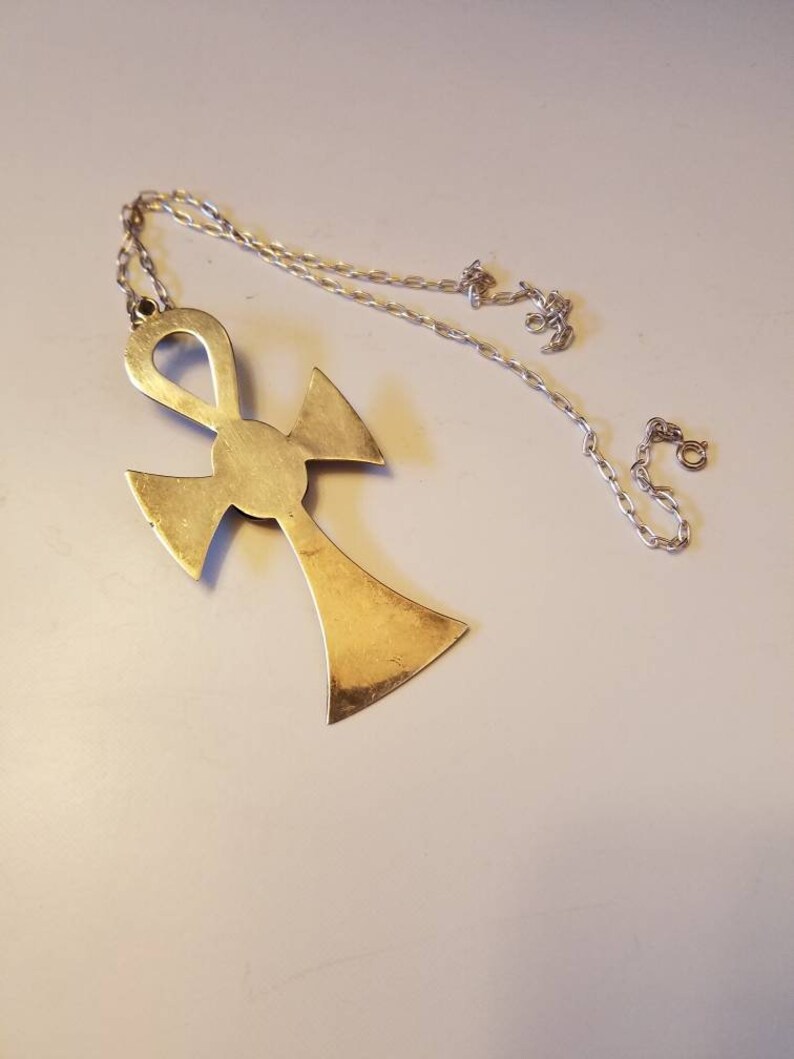 May include: A gold-toned Ankh pendant necklace with a silver chain. The Ankh is a symbol of eternal life in ancient Egyptian mythology.