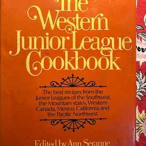 May include: The cover of a vintage orange cookbook titled "The Western Junior League Cookbook". The title is in a yellow font. The text below the title reads "The best recipes from the Junior Leagues of the Southwest, the Mountain states, Western Canada, Mexico, California, and the Pacific Northwest. Edited by Ann Seranne."