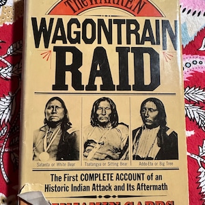 May include: A vintage book cover with a yellow background and black text that reads "The Warren Wagon Train Raid". The cover features three black and white photos of Native American men with the names "Satanta or White Bear", "Tsatangya or Sitting Bear", and "Addo-Eta or Big Tree" underneath each photo. The text "The First Complete Account of an Historic Indian Attack and Its Aftermath" is printed in black below the photos. The author's name, "Benjamin Capps", is printed in red at the bottom of the cover.