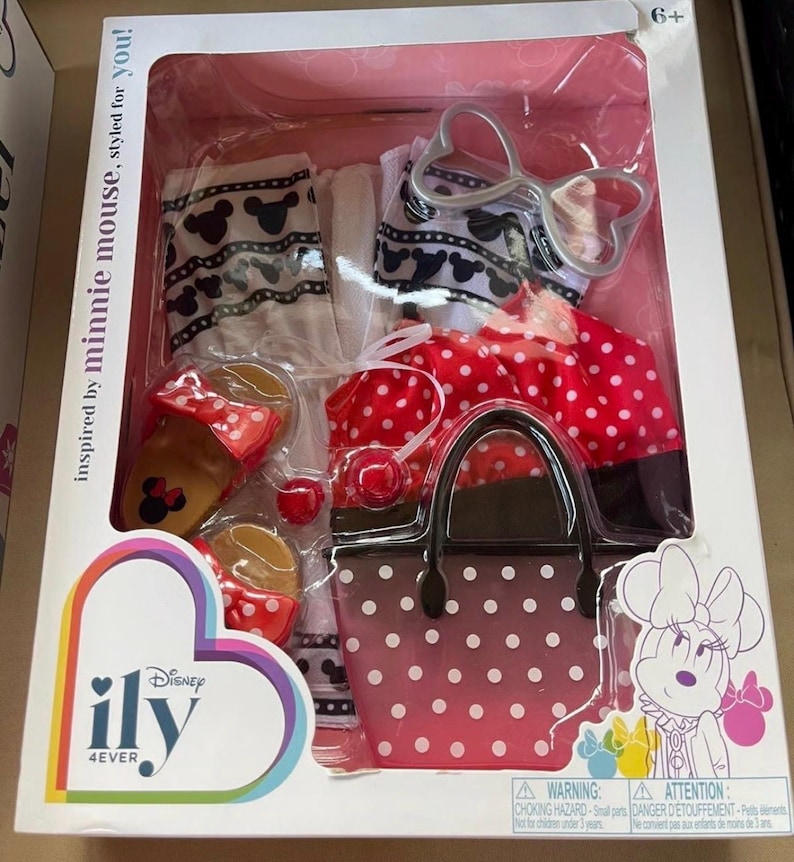 May include: A boxed Minnie Mouse-themed fashion set. The set includes a red polka dot skirt, a matching handbag, sandals, and accessories. The packaging features the text "inspired by minnie mouse, styled for you!" and the Disney "ily 4ever" logo.