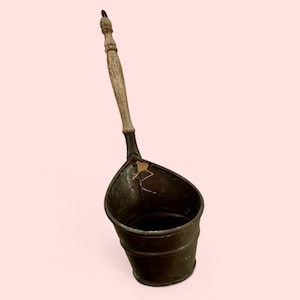 May include: A vintage metal scoop with a wooden handle. The scoop is dark green and has a worn, rustic look. It has a wide, rounded opening and a narrow base.