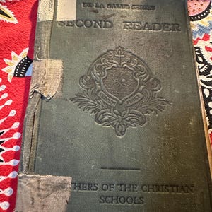 May include: A green, worn book titled "Second Reader" from the De La Salle Series. The book is published by the Brothers of the Christian Schools.