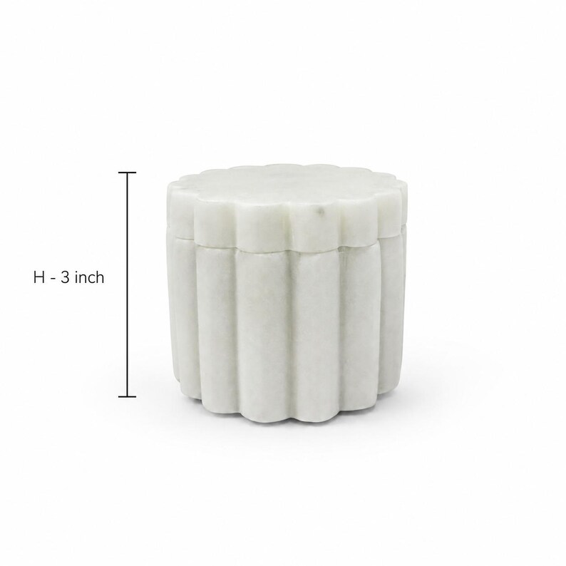 May include: A white marble container with a scalloped, fluted exterior design and a matching lid. The cylindrical vessel features a vertical ribbed pattern around its circumference. A measurement indicator shows a height of 3 inches.
