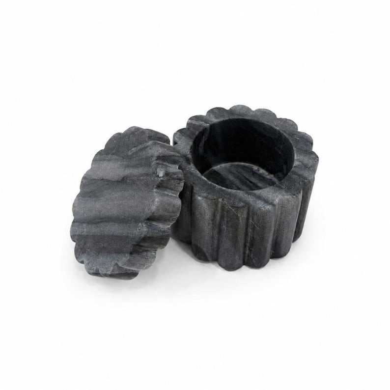 May include: A dark gray marble container with a scalloped, fluted exterior design. The object consists of a cylindrical base with a hollow interior and a separate, matching circular lid with a scalloped edge, both featuring natural stone veining.