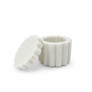 May include: A white marble container with a scalloped, fluted exterior design and a matching circular lid placed beside it. The stone features subtle grey veining throughout the cylindrical body and the edge of the removable lid.