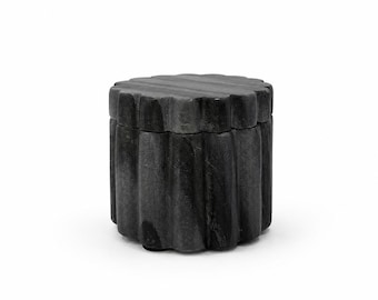 May include: A dark gray stone container with a cylindrical shape and a scalloped, fluted exterior surface. The object features a matching removable lid that sits flush with the vertical, grooved sides, creating a uniform and textured appearance.