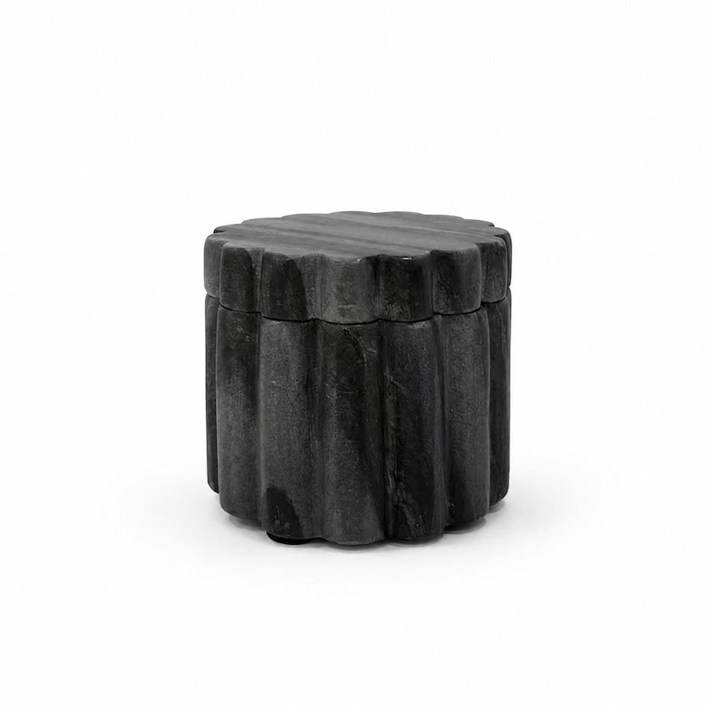 May include: A dark gray stone container with a cylindrical shape and a scalloped, fluted exterior surface. The object features a matching removable lid that sits flush with the vertical, grooved sides, creating a uniform and textured appearance.