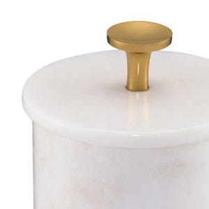 May include: A cylindrical white marble container with a smooth, polished surface and a circular lid. The lid features a centered, solid gold-toned metal knob with a flared base and a flat, circular top, providing a contrast to the stone.