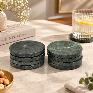 Peut inclure: Deux piles de dessous de verre circulaires en marbre vert foncé avec des motifs de veines naturels. Chaque dessous de verre présente une finition lisse et polie ainsi qu'une forme ronde uniforme. Un dessous de verre est sous un verre strié.