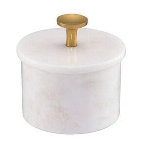May include: A cylindrical white marble container with a smooth, polished finish and subtle light pink veining. The container features a matching circular lid topped with a small, centered, metallic gold-toned knob handle for easy lifting.