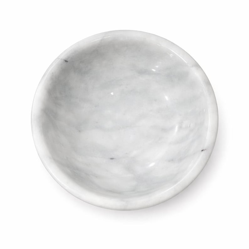 Puede incluir: Un cuenco circular fabricado en m&aacute;rmol blanco con vetas grises naturales por toda la superficie. El cuenco presenta un interior liso y pulido con un borde redondeado, visto directamente desde arriba sobre un fondo blanco liso.