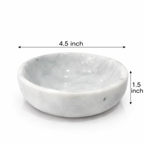 Puede incluir: Un cuenco redondo de m&aacute;rmol blanco con vetas grises. El cuenco presenta una superficie interior y exterior lisa y pulida. El texto indica un di&aacute;metro de 11,43 cm y una altura de 3,81 cm, claramente marcados con flechas para la escala.