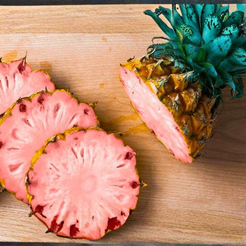 Puede incluir: Rodajas de pi&ntilde;a rosa sobre una tabla de cortar de madera. La pi&ntilde;a tiene una c&aacute;scara amarilla y un interior rosa vibrante. Se ven las hojas verdes y azules de la pi&ntilde;a. Las rodajas est&aacute;n dispuestas para mostrar el color &uacute;nico de la fruta.