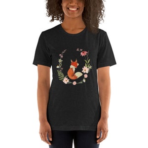 May include: A dark heather grey t-shirt with a graphic of a fox sitting in a circle of flowers. The fox is orange and white, and the flowers are pink, white, and green.