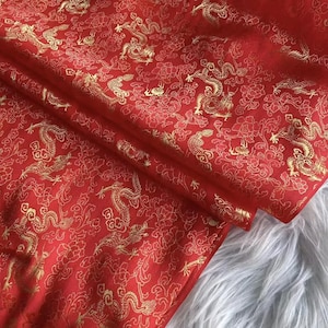 May include: Red fabric with a gold dragon and floral pattern. The fabric is folded, showing the intricate design. The dragons are stylized and detailed, set against a backdrop of flowers.