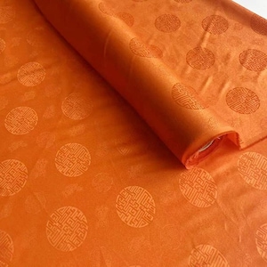 Könnte beinhalten: Orangener Stoff mit einem sich wiederholenden kreisförmigen Muster. Der Stoff ist auf der rechten Seite aufgerollt und zeigt die Textur und das Design. Das Muster besteht aus detaillierten, hellorangenen Kreisen.