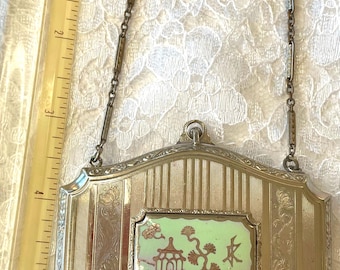 Könnte beinhalten: Eine rechteckige silberfarbene Metalltasche mit Kettenhenkel, verziert mit vertikalen Streifengravuren und einer zentralen rechteckigen Einlage, die eine Pagode und einen Baum in Kupfer auf hellgrünem Grund zeigt, neben einem 14 cm Lineal.