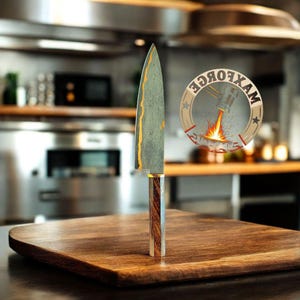 May include: A handcrafted chef's knife with a patterned blade and a wooden handle stands on a wooden cutting board. The blade has gold accents. A circular logo with the text "MAXFORCE" is visible in the background. The knife is designed for kitchen use.