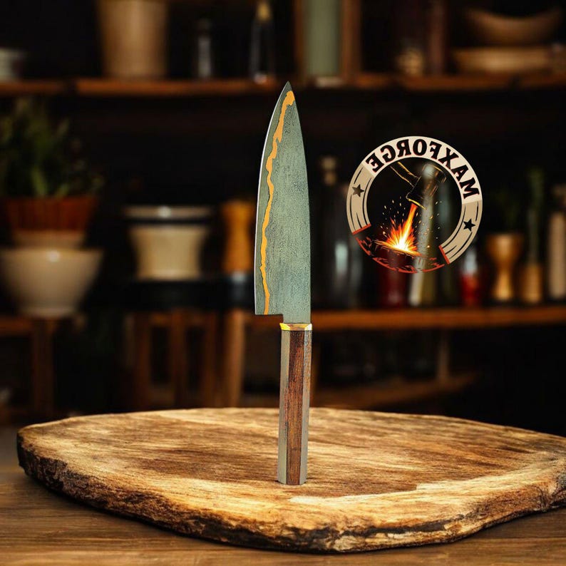 May include: A handcrafted chef's knife with a wooden handle and a blade featuring a unique gold and green pattern. The knife is displayed on a wooden cutting board. A circular logo with the text "MAXFORCE" is visible.