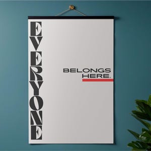 May include: A white poster with the words "EVERYONE BELONGS HERE" in black text. The word "EVERYONE" is stacked vertically on the left side, and "BELONGS HERE" is on the right. A red line underlines "HERE". The poster is hanging on a teal wall.