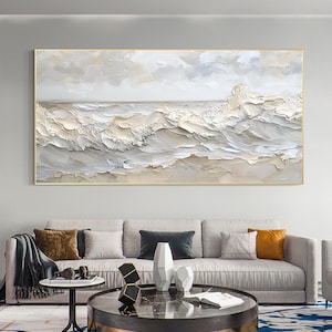 May include: A large, rectangular framed painting depicts a textured ocean scene. The artwork features a palette of white, beige, and gray, with thick brushstrokes creating the illusion of waves and clouds. The frame is a thin, gold color.