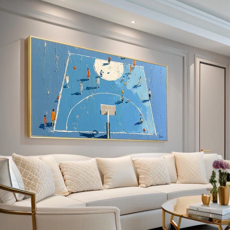 May include: A large, rectangular painting depicts a basketball court in shades of blue with players in action. The artwork features a textured, impasto style with a gold frame, creating a modern aesthetic. The painting hangs above a white sofa in a living room setting.