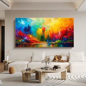 May include: A vibrant abstract landscape painting with a gold frame. The artwork features a colorful array of blues, greens, yellows, oranges, and reds, depicting a scene with a body of water reflecting the vivid hues of the sky and trees.