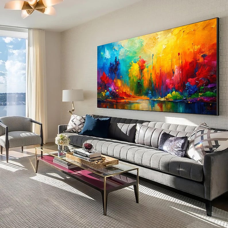 May include: A large, vibrant abstract painting dominates a modern living room. The artwork features a colorful landscape with bold strokes of red, yellow, blue, and green. A gray sofa with decorative pillows and a glass coffee table complete the scene.