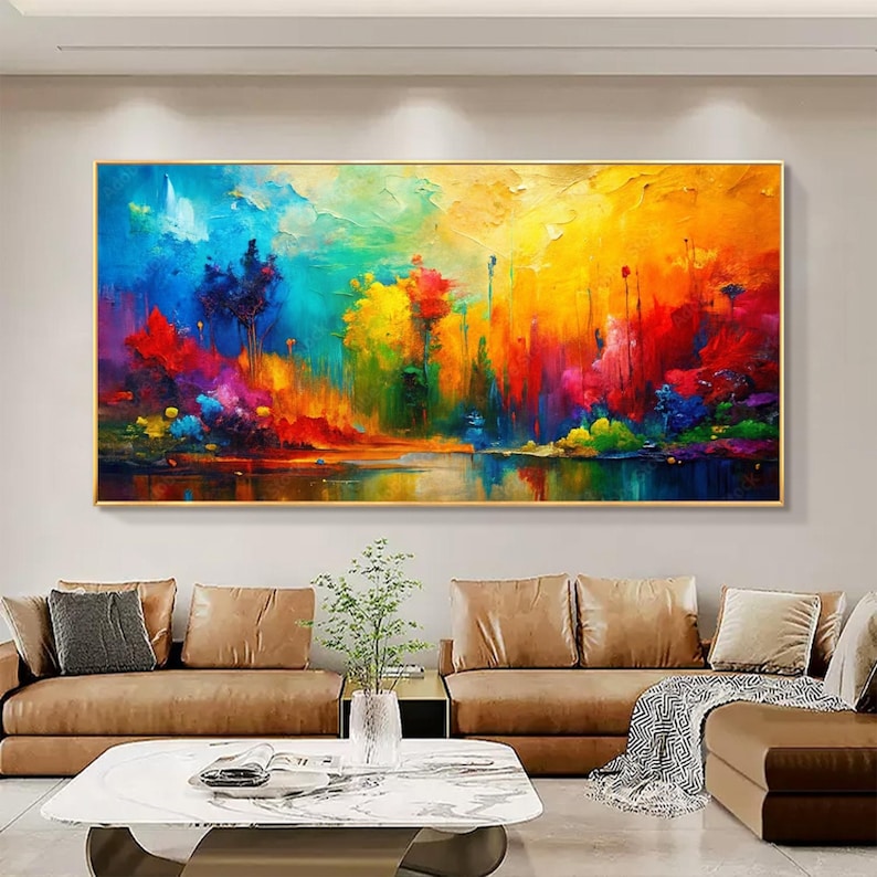 May include: A vibrant abstract landscape painting with a gold frame. The artwork features a colorful scene with a lake reflecting the sky and trees. The color palette includes blues, yellows, reds, and greens, creating a lively and dynamic composition. The painting is displayed above a brown sofa.