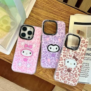 Può includere: Tre custodie per telefono con disegni di personaggi dei cartoni animati. Le custodie presentano motivi leopardati rosa, viola e bianchi. Ogni custodia ha un design di personaggio diverso, tra cui un coniglietto, un orso e un gatto. Le custodie sono su una superficie di legno.