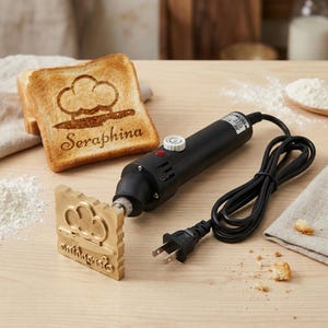 Könnte beinhalten: Ein schwarzer Brennstempel mit Holzgriff und quadratischem Messingstempel. Der Stempel befindet sich neben einer Toastscheibe mit Wolken- und Kochmützen-Design und dem Namen "Seraphina". Das Bügeleisen ist an eine Steckdose angeschlossen.