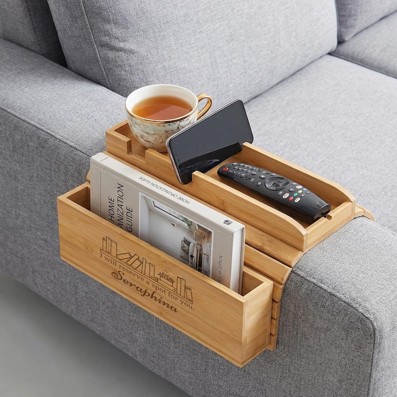 May include: A bamboo sofa arm tray with compartments for a teacup, phone, remote, and book. The book is titled "HOME ORGANIZATION GUIDE" and the tray has the text "I will reserve a spot for you. Seraphina."