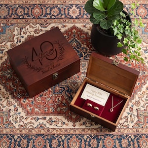 May include: A dark wood keepsake box with a closed lid engraved with 40 years, 1986-2026, and Mia & Claire. An open matching box contains two gold rings and a gold necklace with a red stone, plus a card reading Happy 40th Wedding Anniversary.