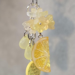 May include: A silver-toned metal keychain featuring translucent yellow flower charms, two small pale yellow teardrop beads, a realistic yellow lemon slice charm, and a round yellow disc with the text You are my sunshine my only sunshine.