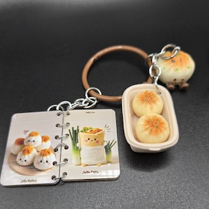 May include: A set of food-themed keychains. One keychain features a small notebook with illustrations of cartoon dumplings and the text "Jelly Pets" and "Jelly Belly". Another keychain has two miniature dumplings in a small container.