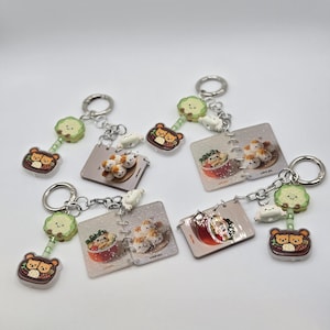 May include: A collection of keychains with various food-themed designs. Each keychain features a small, square charm with a food illustration, a bear-shaped charm, and a green cloud charm. The keychains are attached to silver key rings.