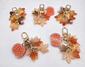 May include: Five keychains featuring gold-tone lobster clasps, each adorned with various resin charms including orange pumpkins with white stripes, brown acorns, and multiple maple leaves in shades of yellow, orange, and brown, arranged in clusters.