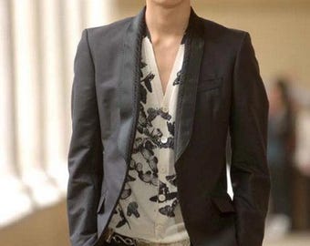 Könnte beinhalten: Ein dunkelgrauer Blazer mit schwarzen Revers und passender schwarzer Hose. Darunter ein weißes Button-up-Hemd mit einem schwarzen Schmetterlingsmuster. Das Outfit ist ein stilvolles Ensemble, das für formelle oder halbformelle Anlässe geeignet ist.