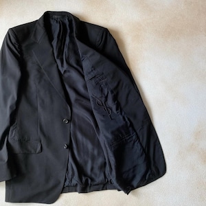 May include: A black blazer with a two-button closure and a notched lapel. The interior lining is black, and the blazer has a pocket on the left side. The blazer is made of a smooth fabric.