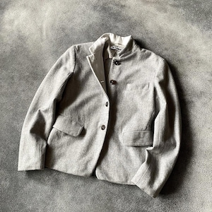 Peut inclure: Un blazer gris clair avec un col blanc et trois boutons marron foncé. Le blazer a deux poches avant et une coupe ajustée. L'étiquette "Jil Sander" est visible sur le col. La veste est en tissu doux et texturé.