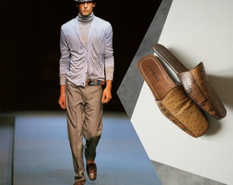 Könnte beinhalten: Ein Modebild mit einem Model in einer hellblauen Strickjacke, grauer Hose und einem Fedora. Braune Leder-Slipper mit der Marke "PRADA" werden auf einer weißen Oberfläche präsentiert. Die Schuhe haben ein strukturiertes Design.