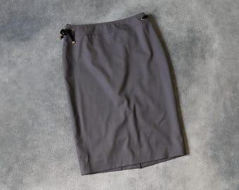 Könnte beinhalten: Ein grauer Bleistiftrock mit gerader Silhouette. Der Rock hat eine hohe Taille und schwarze Kordelzüge mit goldfarbenen Akzenten an der Taille. Der Rock ist aus einem glatten, einfarbigen Stoff gefertigt.