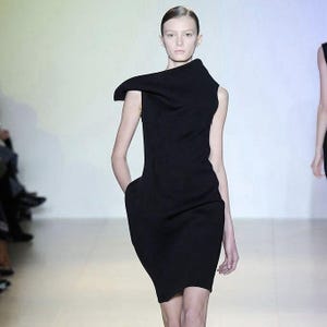 May include: A black sleeveless dress featuring a structured, asymmetrical folded neckline that extends over one shoulder. The garment has a fitted bodice and a skirt that tapers slightly toward the hem, creating a clean, solid-colored silhouette.