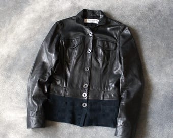 Könnte beinhalten: Eine schwarze Lederjacke mit Kragen, Knopfleiste auf der Vorderseite und zwei Brusttaschen mit Klappen. Der untere Teil der Jacke besteht aus einem gerippten schwarzen Strickstoff. Ein Christian Dior-Etikett ist am Halsausschnitt zu sehen.