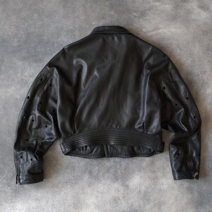 May include: A black leather jacket, cropped in style. It has a ribbed waistband and cuffs, a classic collar, and perforated detailing on the sleeves. The rear view highlights the jacket's design and construction.