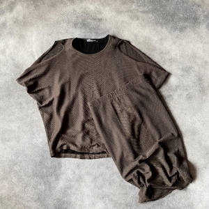 May include: A brown textured top with short sleeves and a round neckline. The top features a unique draped design and a contrasting black inner layer. The fabric has a subtle pattern, adding visual interest. The top is laid flat on a grey surface.
