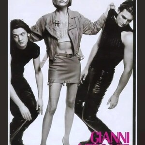 May include: Black and white fashion advertisement featuring three people. A woman in a cropped jacket and skirt stands between two people in black clothing. The text "GIANNI VERSACE" is displayed in pink and white.